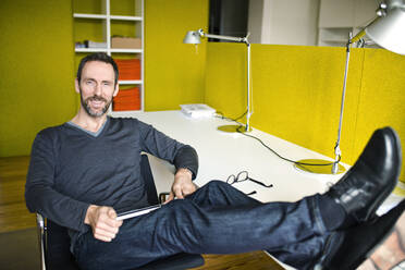 Porträt eines lächelnden Geschäftsmannes im Büro mit Füßen auf dem Schreibtisch - MIK00012