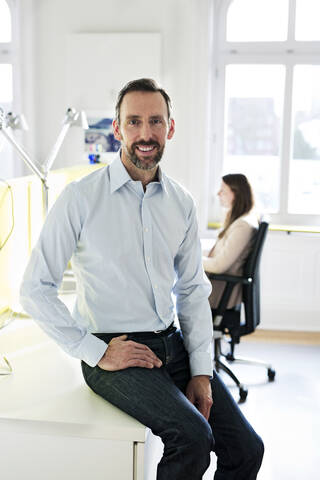 Porträt eines lächelnden Geschäftsmannes im Büro mit Angestellten im Hintergrund, lizenzfreies Stockfoto
