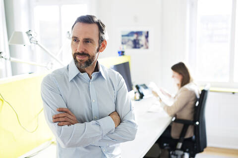 Porträt eines selbstbewussten Geschäftsmannes im Büro mit einem Angestellten im Hintergrund, lizenzfreies Stockfoto