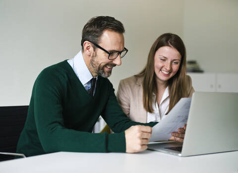 Lächelnder Geschäftsmann und Angestellter mit Laptop und Dokumenten bei der Arbeit am Schreibtisch im Büro, lizenzfreies Stockfoto