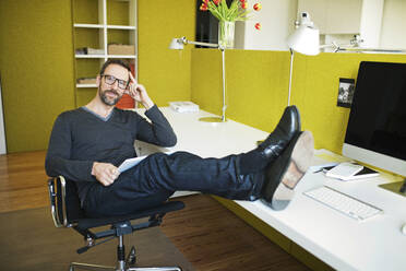 Portrait of smiling businessman in office with feet on desk - MIK00050