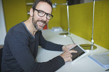 Portrait of smiling businessman using tablet at desk in office - MIK00051