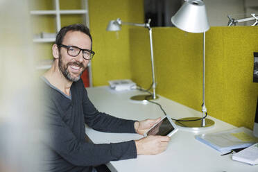 Portrait of smiling businessman using tablet at desk in office - MIK00052