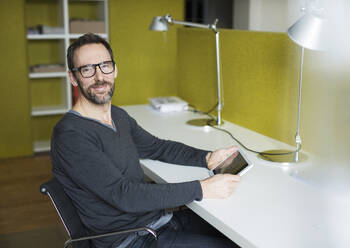 Portrait of confident businessman using tablet at desk in office - MIK00053