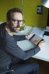 Porträt eines selbstbewussten Geschäftsmannes, der ein Tablet am Schreibtisch im Büro benutzt - MIK00055