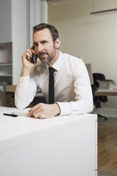 Businessman talking on the phone at desk in office - MIK00060