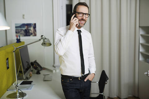 Lächelnder Geschäftsmann beim Telefonieren im Büro, lizenzfreies Stockfoto
