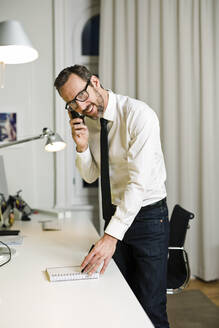 Lächelnder Geschäftsmann beim Telefonieren im Büro - MIK00066