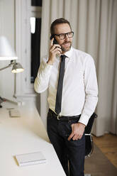 Lächelnder Geschäftsmann beim Telefonieren im Büro - MIK00067