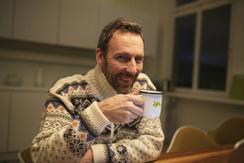 Porträt eines glücklichen Geschäftsmannes mit Tasse, der zu Hause am Tisch sitzt, lizenzfreies Stockfoto