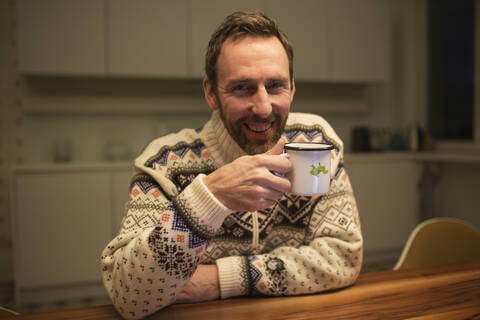 Porträt eines glücklichen Geschäftsmannes mit Tasse, der zu Hause am Tisch sitzt, lizenzfreies Stockfoto