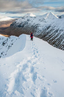 Eine Wanderin beim Abstieg vom Gipfel des Stob Dubh auf Buchaille Etive Beag an einem klaren Wintertag, Highlands, Schottland, Vereinigtes Königreich, Europa - RHPLF11823