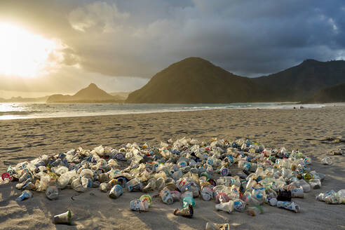 Haufen von Plastikmüll, der bei Sonnenuntergang am Strand von Selong Belanak auf Lombok, Indonesien, Südostasien, Asien, in den Sand gekippt wird - RHPLF11953