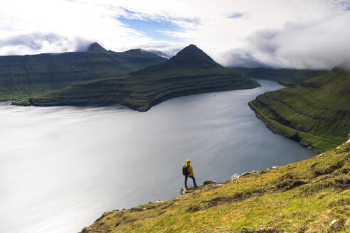 Wanderer auf Felsen schaut auf die Fjorde, Funningur, Insel Eysturoy, Färöer Inseln, Dänemark, Europa - RHPLF12098