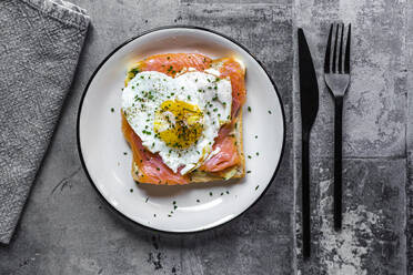 Direkt über der Aufnahme von getoastetem Brot mit Lachs und herzförmigem Spiegelei in einem Teller auf dem Tisch - SARF04343