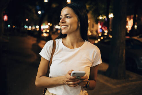 Junge Frau benutzt Smartphone in der nächtlichen Stadt - OYF00064