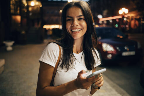 Junge Frau benutzt Smartphone in der nächtlichen Stadt - OYF00074