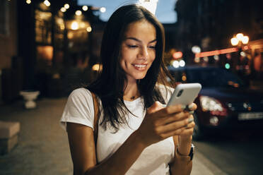 Junge Frau benutzt Smartphone in der nächtlichen Stadt - OYF00075
