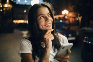 Junge Frau, die nachts in der Stadt ihr Smartphone benutzt und nach oben schaut - OYF00077
