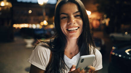 Junge Frau benutzt Smartphone in der nächtlichen Stadt - OYF00080