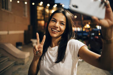 Young woman using smartphone in the city at night, taking a selfie - OYF00081