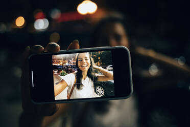 Junge Frau, die nachts in der Stadt ein Smartphone benutzt und ein Selfie macht - OYF00083