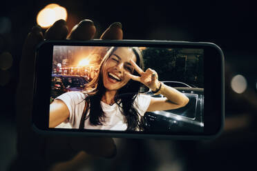 Junge Frau, die nachts in der Stadt ein Smartphone benutzt und ein Selfie macht - OYF00084