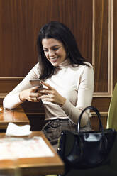Lächelnde Geschäftsfrau mit Handy in einem Restaurant - JSRF00603