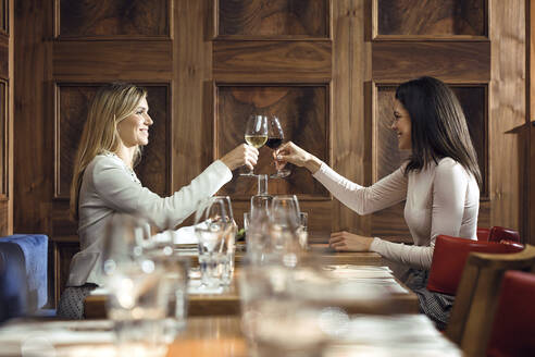 Two businesswomen clinking wine glasses in a restaurant - JSRF00610