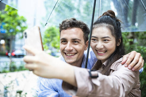 Happy couple with umbrella taking a selfie in Ginza, Tokyo, Japan - MCVF00021