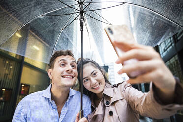 Glückliches Paar mit Regenschirm macht ein Selfie in Ginza, Tokio, Japan - MCVF00025