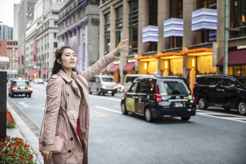 Junge Frau ruft ein Taxi in einer Straße in Ginza, Tokio, Japan - MCVF00033