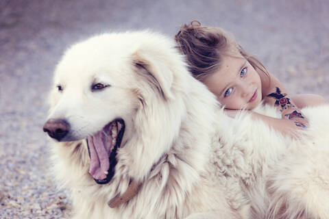 Porträt eines kleinen Mädchens, das einen gähnenden weißen Hund knuddelt, lizenzfreies Stockfoto