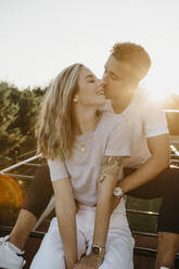 Young couple kissing each other on a climbing frame at sunset - LHPF00852