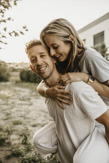 Porträt eines jungen lächelnden Paares, der Mann trägt die Frau auf dem Rücken - LHPF00856