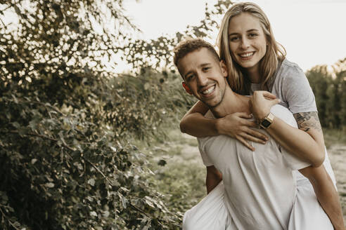 Porträt eines jungen lächelnden Paares, der Mann trägt die Frau auf dem Rücken - LHPF00857