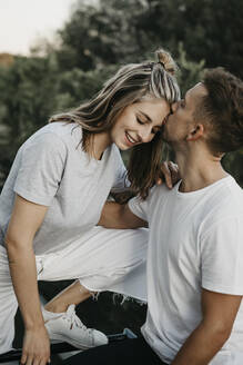 Porträt eines jungen lächelnden Paares, der Mann küsst sie auf die Stirn - LHPF00867