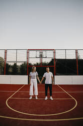 Junges Paar auf einem Basketballplatz, Hände haltend - LHPF00882