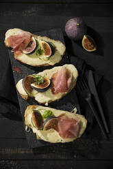 High angle view of baked cheese bread with fig slices and ham served on table - MAEF12943