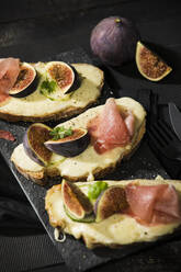 Close-up of baked cheese bread with fig slices and ham served on table - MAEF12945