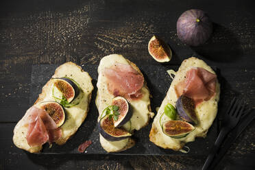 High angle view of baked cheese bread with fig slices and ham served on wooden table - MAEF12947