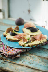 High angle view of baked cheese bread with fig slices and ham served in plate on wooden table - MAEF12950