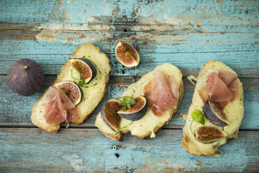 Directly above shot of baked cheese bread with fig slices and ham served on wooden table - MAEF12951