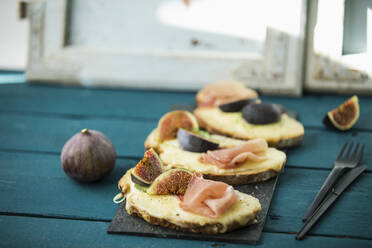 Nahaufnahme von gebackenem Käsebrot mit Feigenscheiben und Schinken auf einem Holztisch - MAEF12952