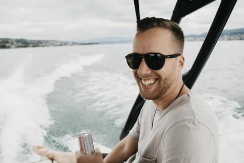 Happy man wearing sunglasses on a boat trip on a lake - LHPF00905
