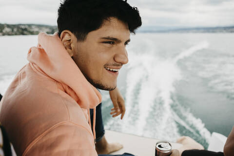 Fröhlicher junger Mann bei einem Drink während einer Bootsfahrt auf einem See, lizenzfreies Stockfoto