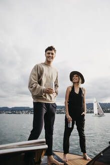 Glückliches junges Paar bei einem Drink während einer Bootsfahrt auf einem See - LHPF00914