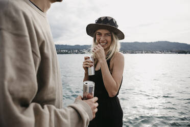 Glückliches junges Paar bei einem Drink an einem See - LHPF00920