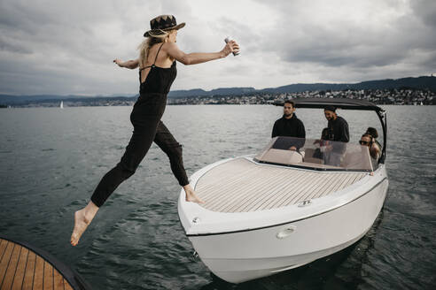 Junge Frau springt auf ein Boot auf einem See - LHPF00922