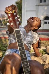 Lächelnde Frau mit Gitarre sitzend im Freien - VEGF00712